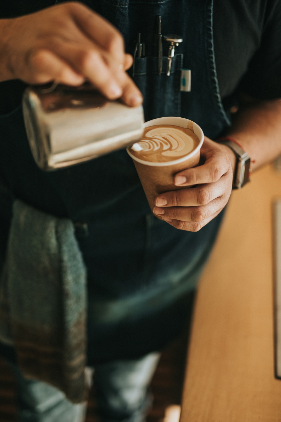A barista pouring latte art into a Daai Koffie takeaway cup